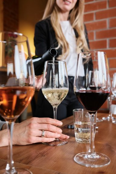 Sommelier Wine Service Sommelier pouring wine into tall glasses arranged along a brick wall bar.